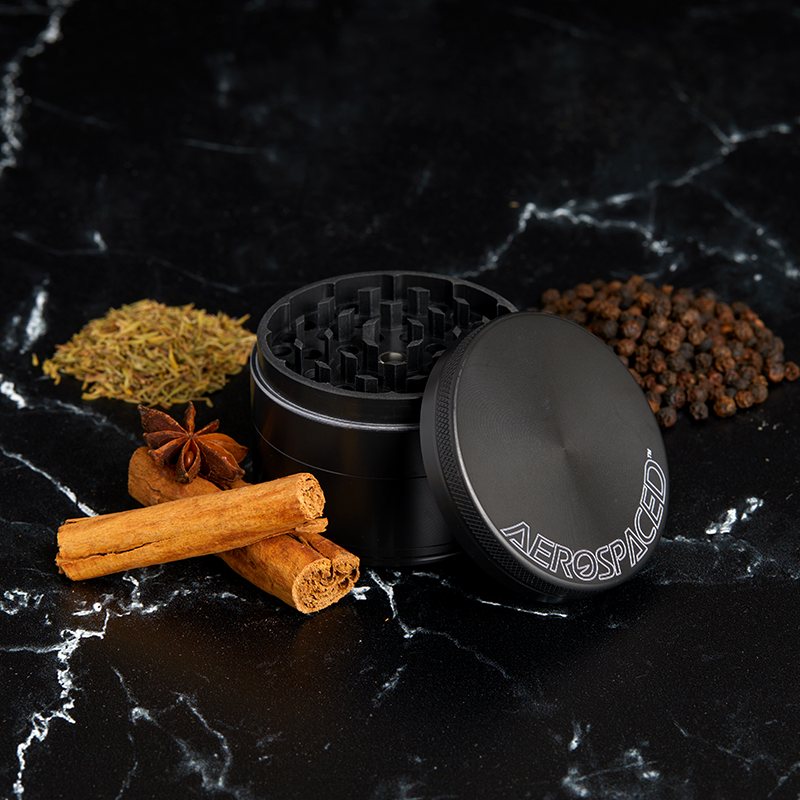 Graphite 4-piece AEROSPACED grinder surrounded by whole spices